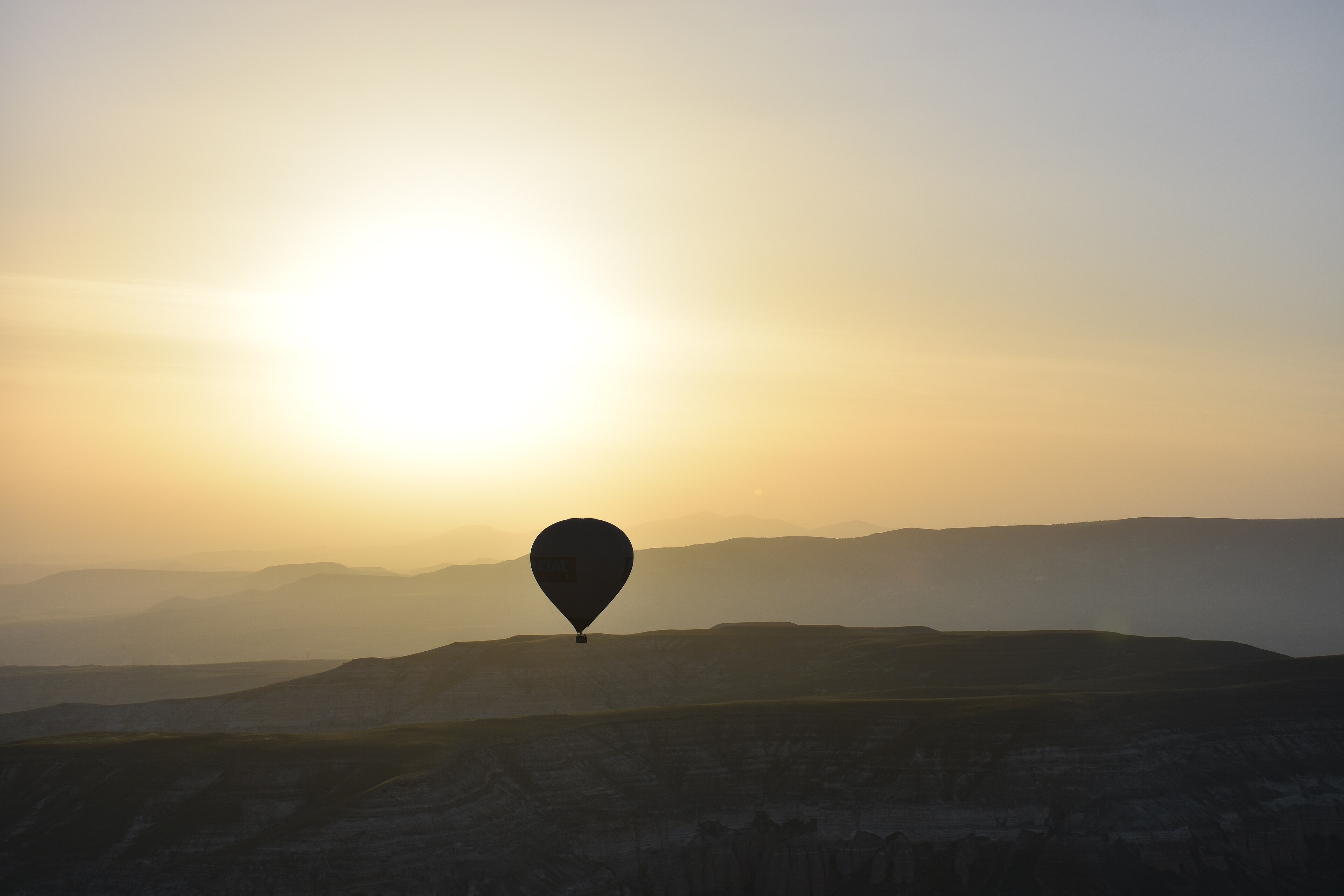 Kapadokya'da gün doğumunda vadilerin üzerinde süzülen tek bir sıcak hava balonu